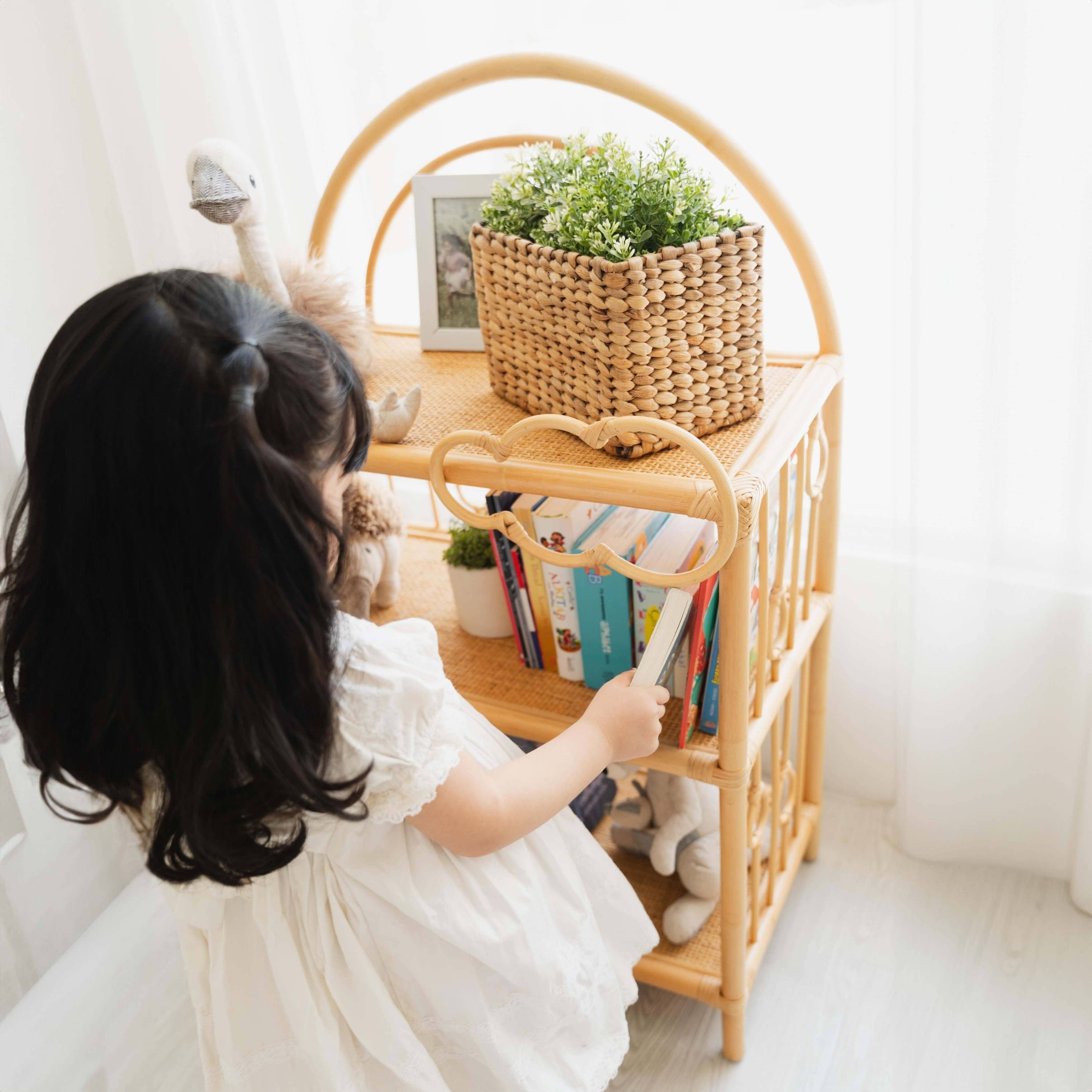 Child taking a book from the After the Rain Shelf by MOMIJI in an indoor setting.