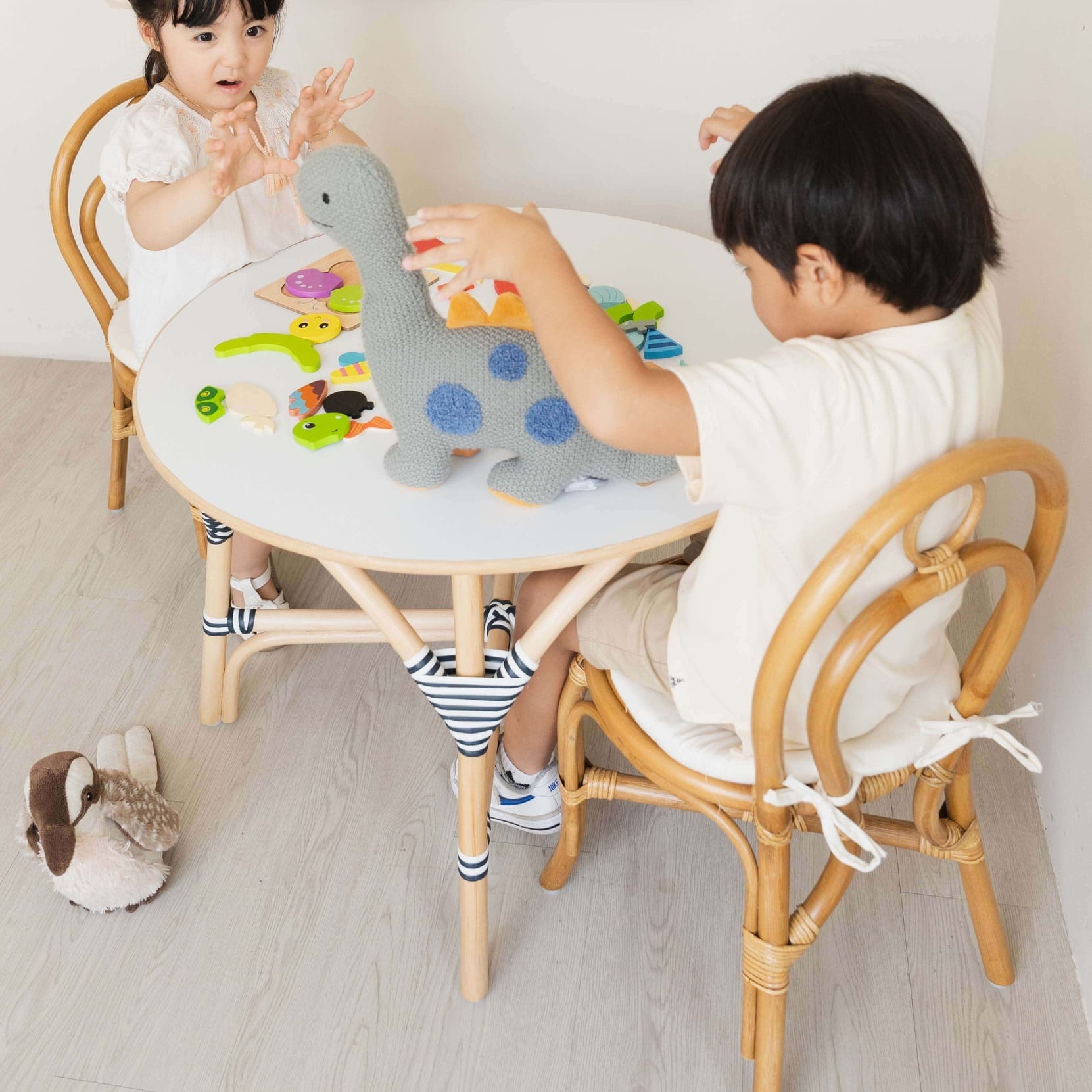 Two children sitting on the Amélie Kids Chair by MOMIJI playing with a dinosaur toy at a round table.