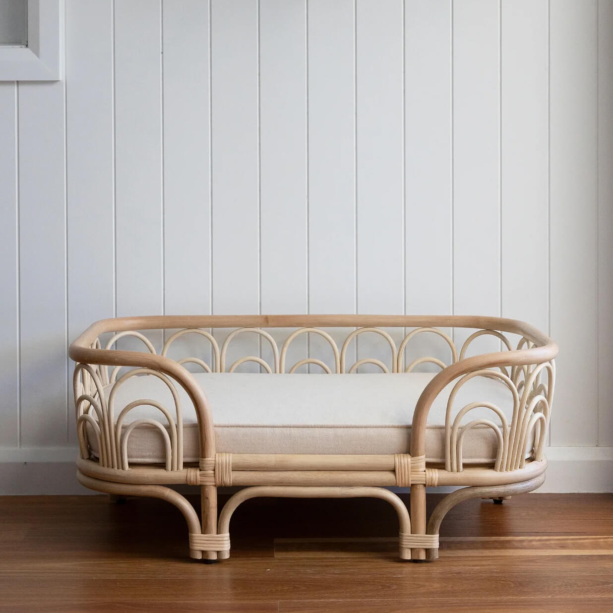 Wicker Amber Pet Bed by MOMIJI with a white cushion placed on a wooden floor.