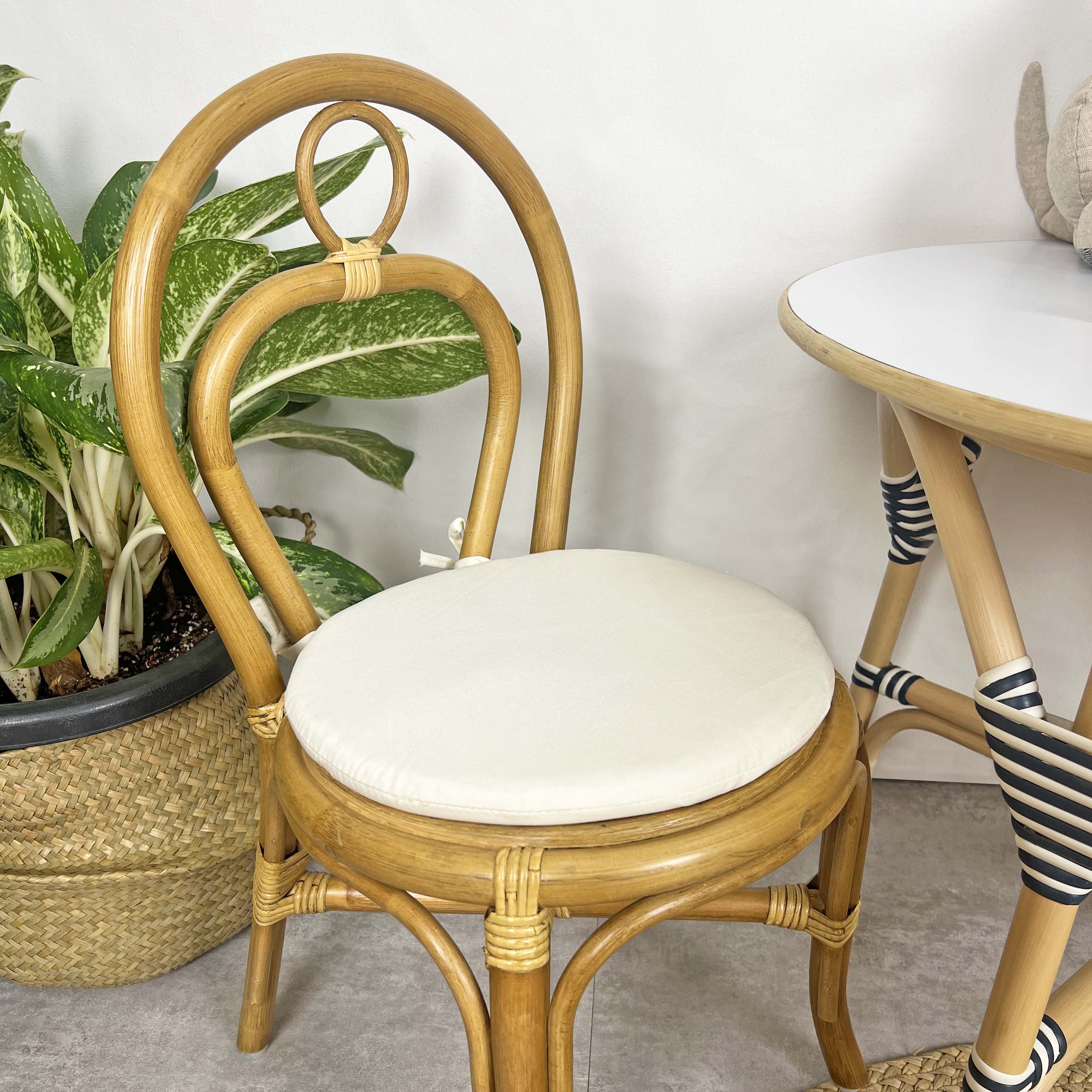 Close-up of the seat and backrest detail of the handcrafted rattan wicker Amélie Kids Chair by MOMIJI in a room with potted plants.