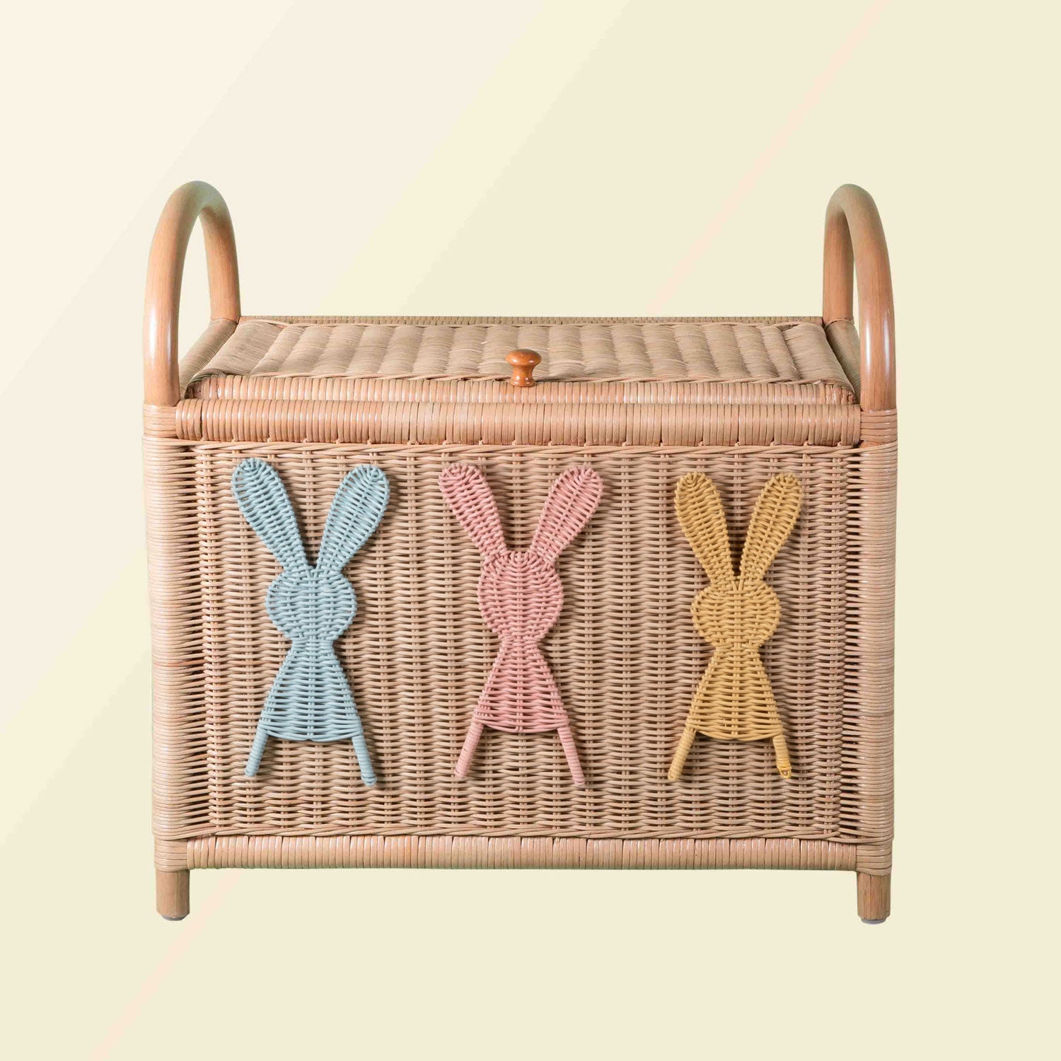 Wicker rattan toy chest with rabbit appliqués and integrated handles and lid knob closure on a neutral background