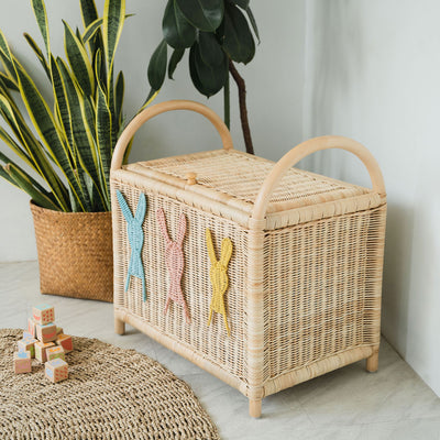 Wicker rattan toy chest with pastel colored bunny decor, integrated handles for easy relocation and handling, and a knob closure on the lid
