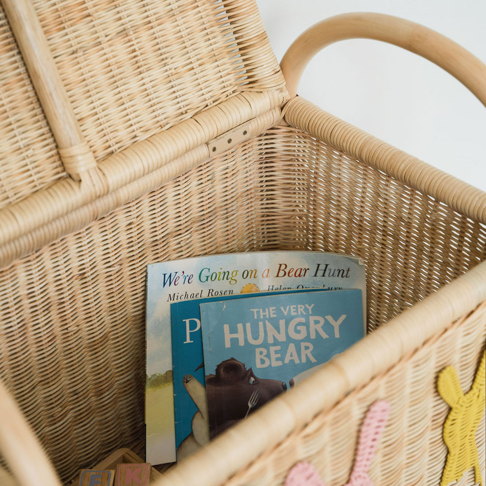 Close-up of children's books inside a rattan wickertoy trunk chest by MOMIJI against a white interior wall