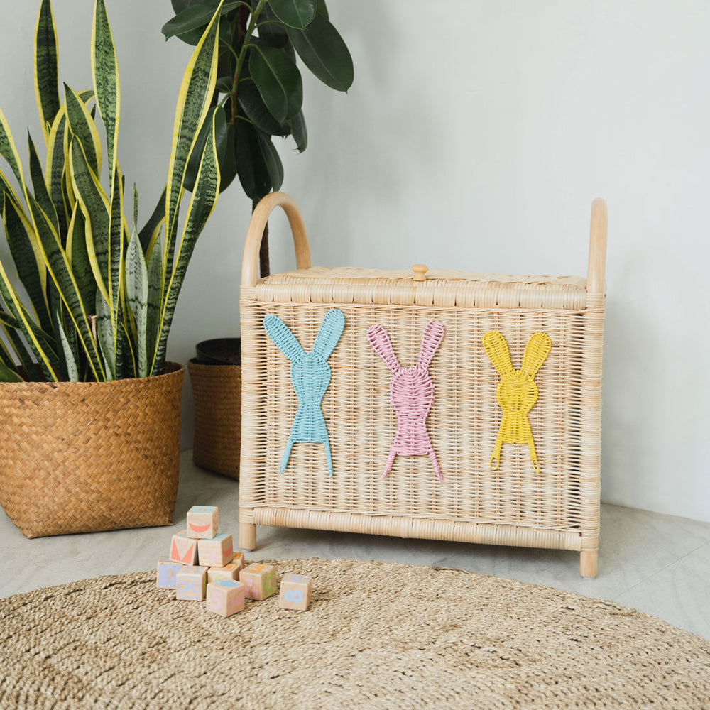 Wicker rattan toy trunk by MOMIJI placed on a light floor next to a plant, woven mat and children’s blocks in a playroom