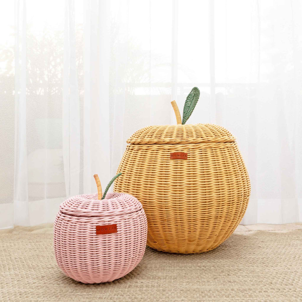 A front view of a small sized pink apple rattan storage basket next to a medium sized natural apple rattan storage basket by MOMIJI.