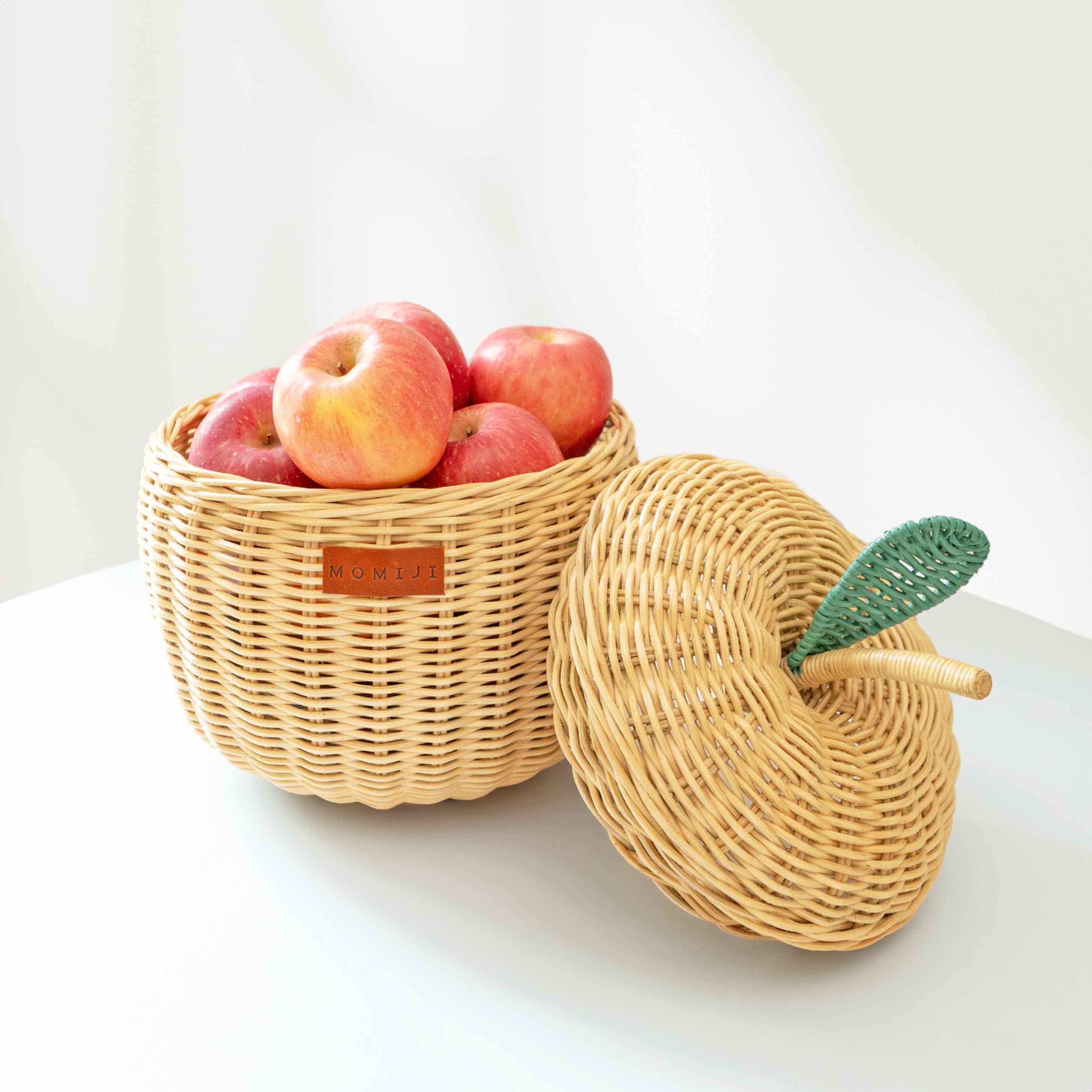 An opened small sized natural apple rattan storage basket by MOMIJI, full with fresh apples inside the basket with lid leaning beside the rattan basket.