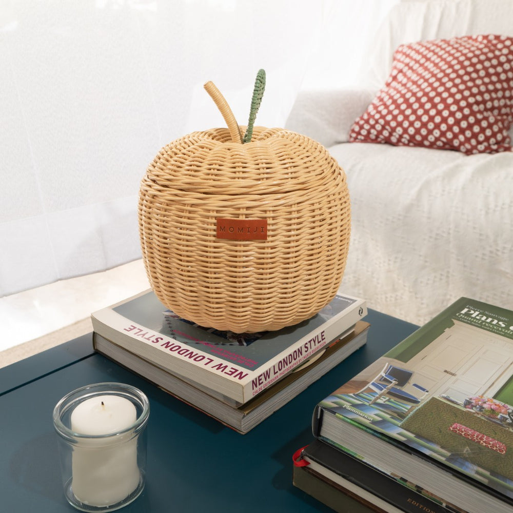 Wicker apple rattan storage basket by MOMIJI on books with a candle and pillow in the background.