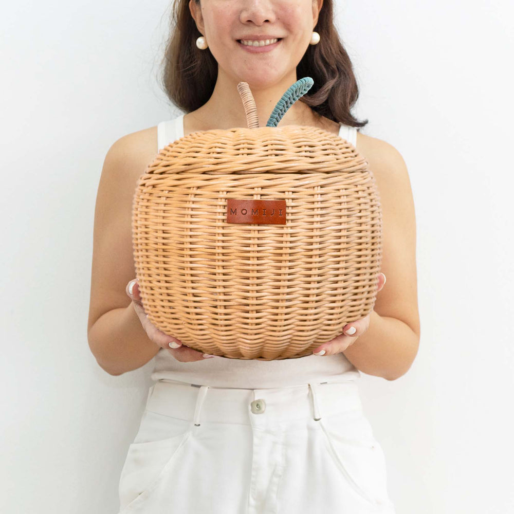 Woman holding a small sized natural apple rattan storage basket by MOMIJI.