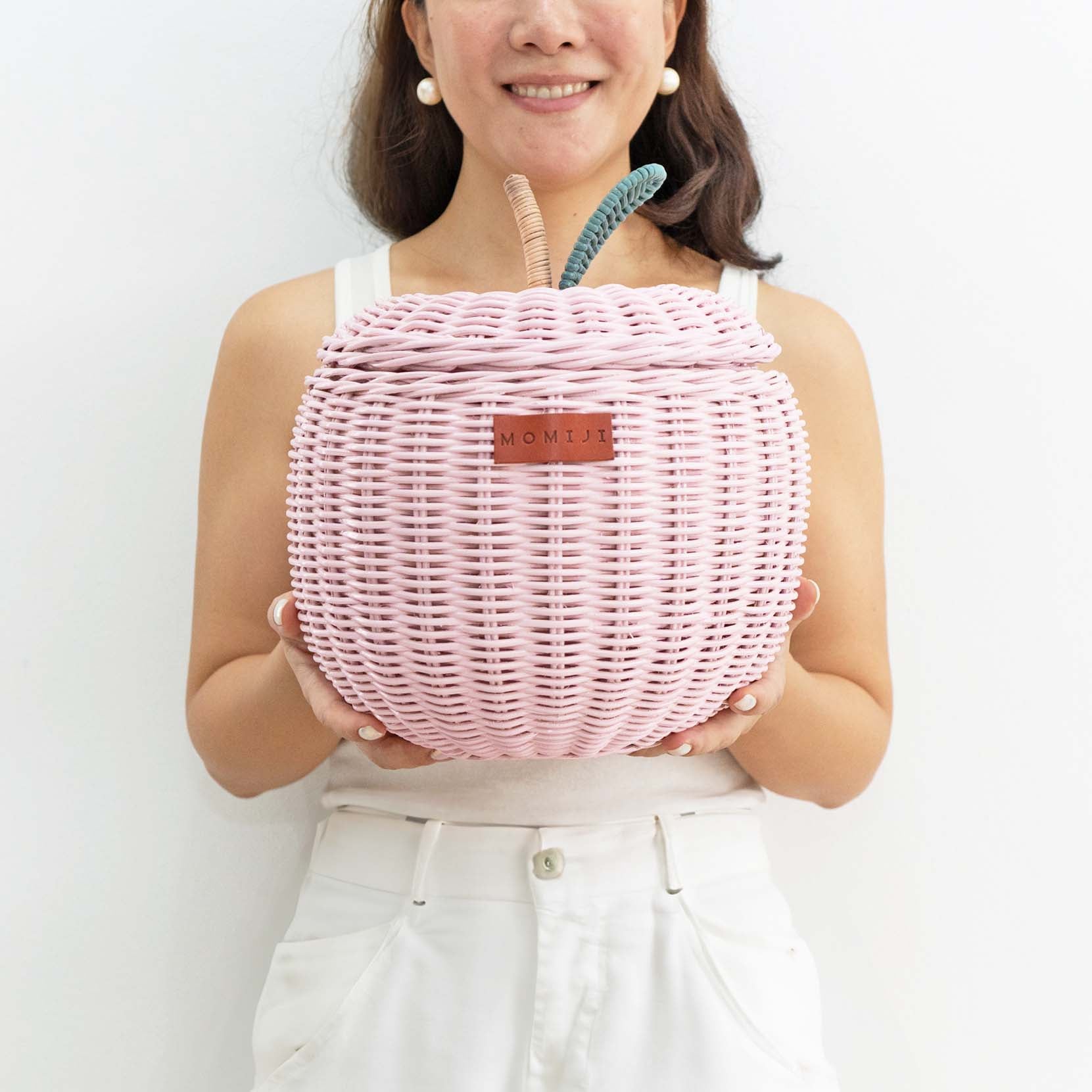 Woman holding a small sized pink apple rattan storage basket by MOMIJI.