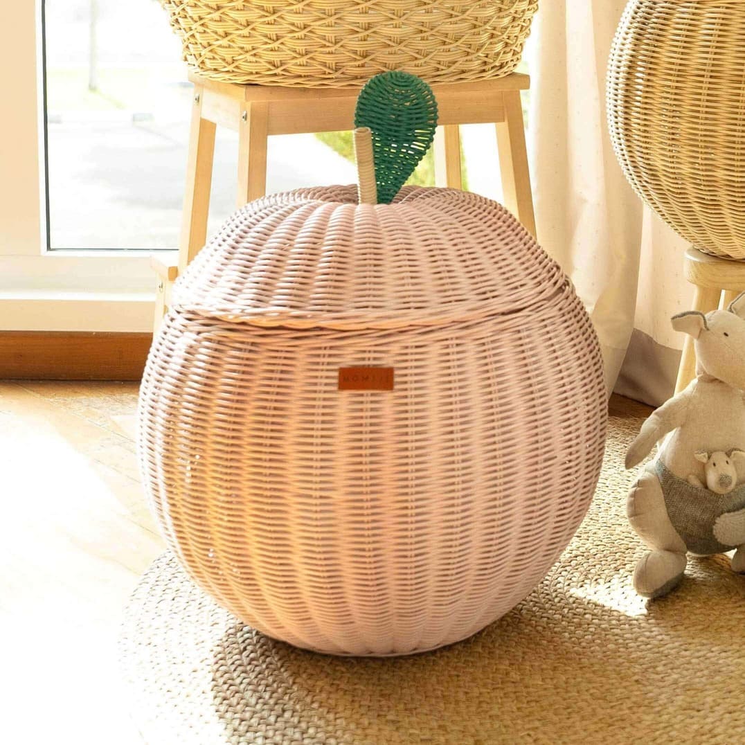 Close up front view of a pink apple rattan storage basket by MOMIJI next to a stuffed toy.