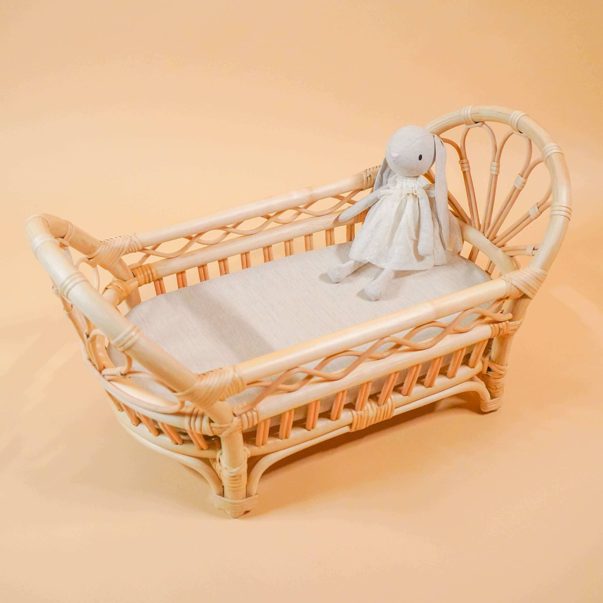 Front view of the Arya Doll Bed by MOMIJI, featuring a full handwoven rattan bed and frame, with a bunny doll resting inside on a cream cushion.