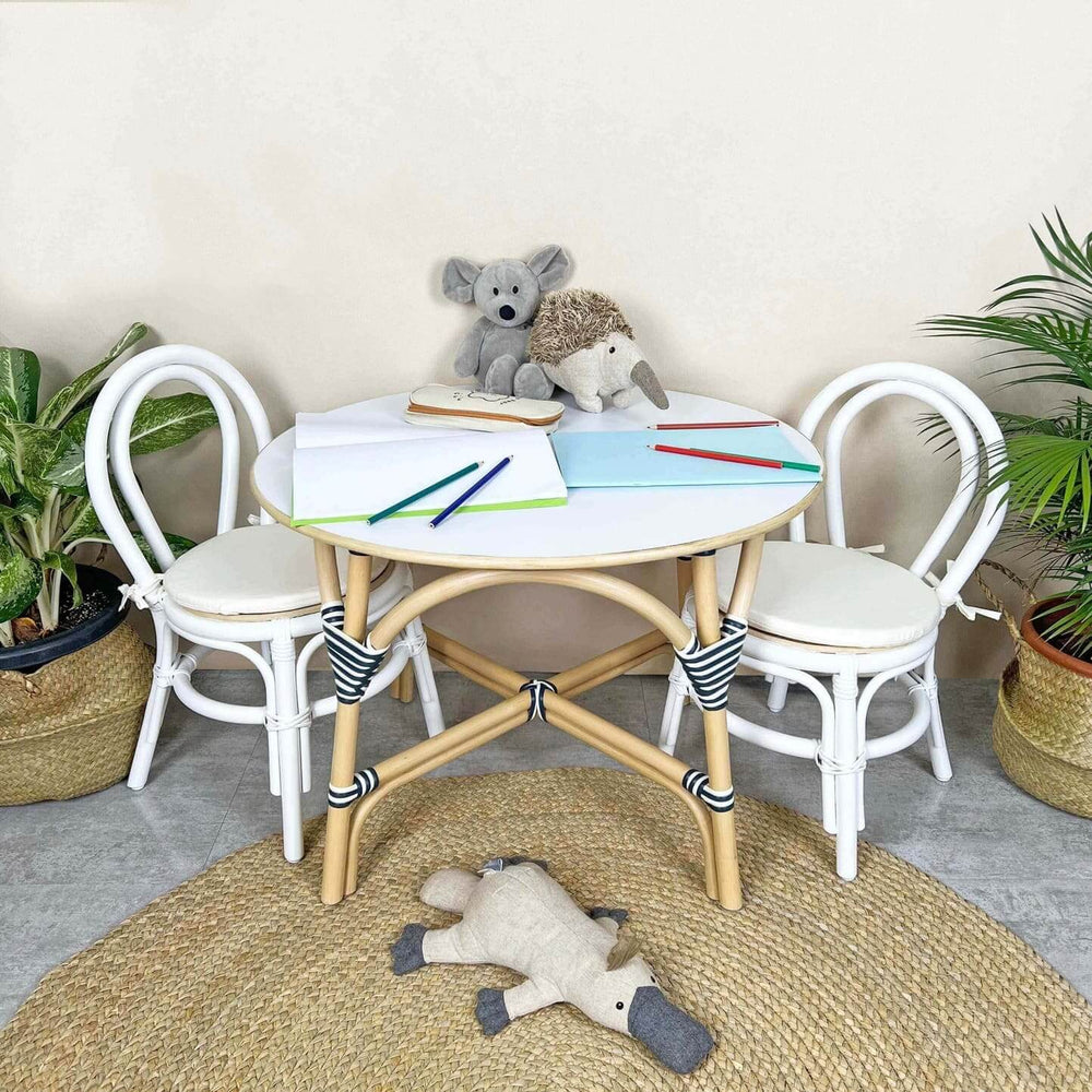 Aulia Kids Chairs by MOMIJI placed beside a rattan table with stationery and toys in a room with plants.