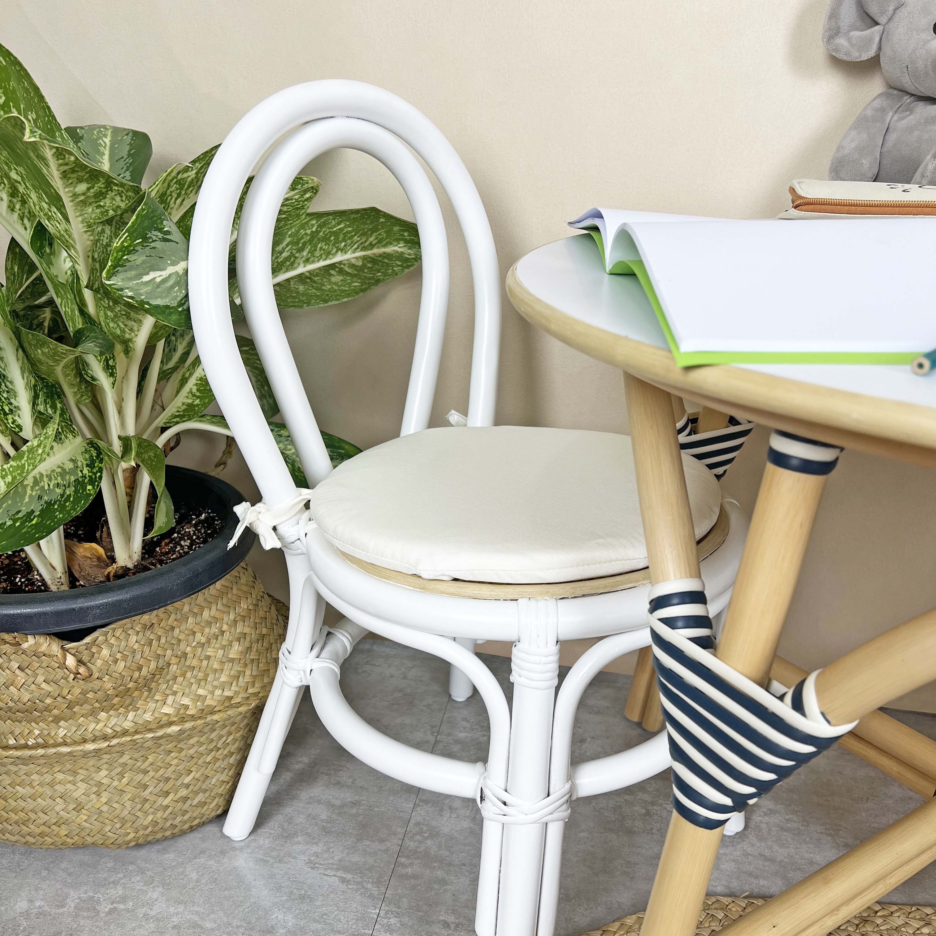 Aulia Kids Chair by MOMIJI with a white cushion placed in front of an Aulia Kids Table in a room with plants, highlighting its sturdy rattan frame with reinforced binding designed for safe and child-friendly support.