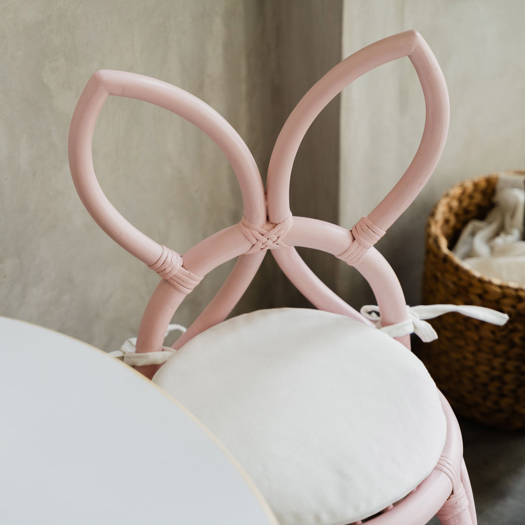 Top view of the handcrafted pink rattan Butterfly Kids Chair by MOMIJI, highlighting the removable white cushion and butterfly-wing shaped backrest, paired with an Aulia Kids Table featuring a laminated tabletop designed for durability and easy cleaning.