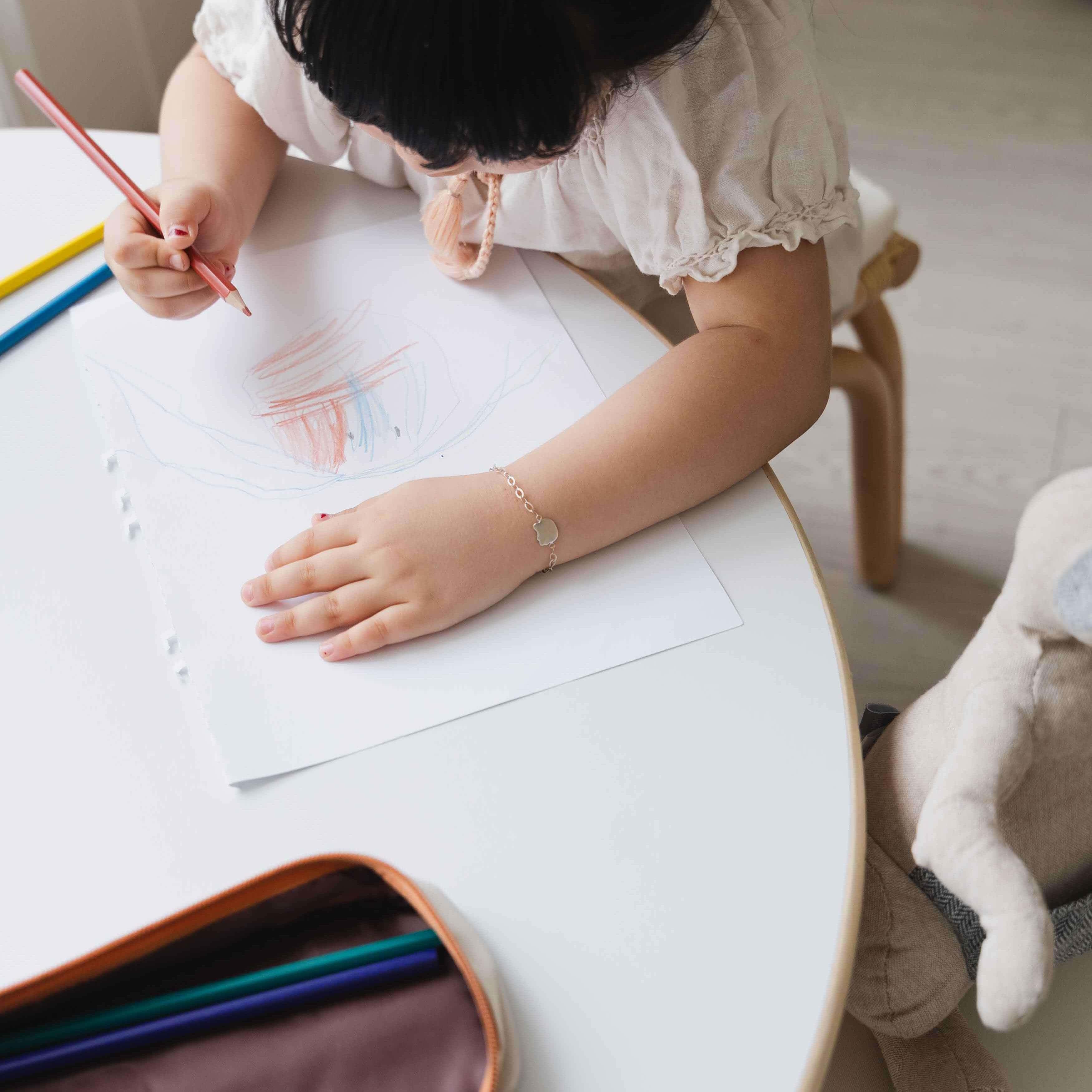 Top view close-up of a child coloring on the Aulia Kids Table by MOMIJI, showing the tabletop surface.