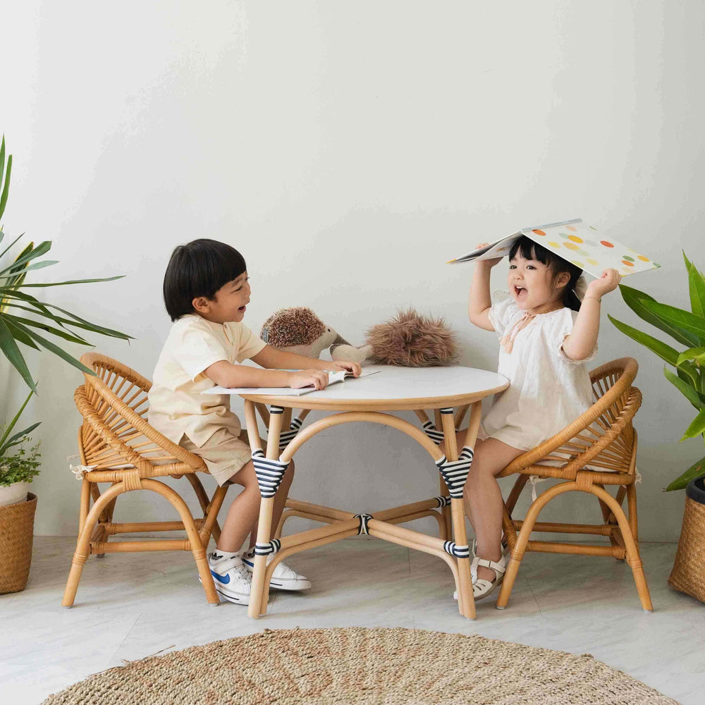 Two children sitting on rattan chairs and laughing around the Aulia Kids Table – Medium by MOMIJI.