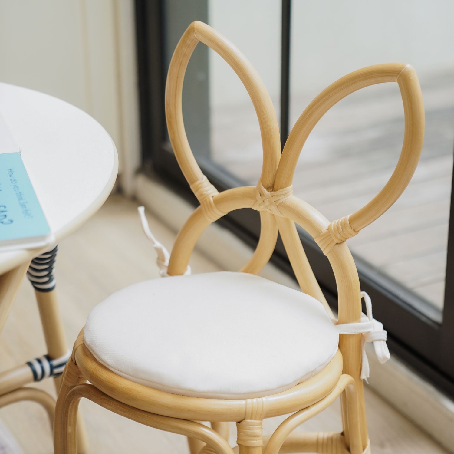 A front view of the handcrafted rattan wicker Aulia Kids Table (Medium) paired with Butterfly Kids Chairs (Natural) by MOMIJI, showcasing the butterfly-shaped backrests and removable cushioned seats. 