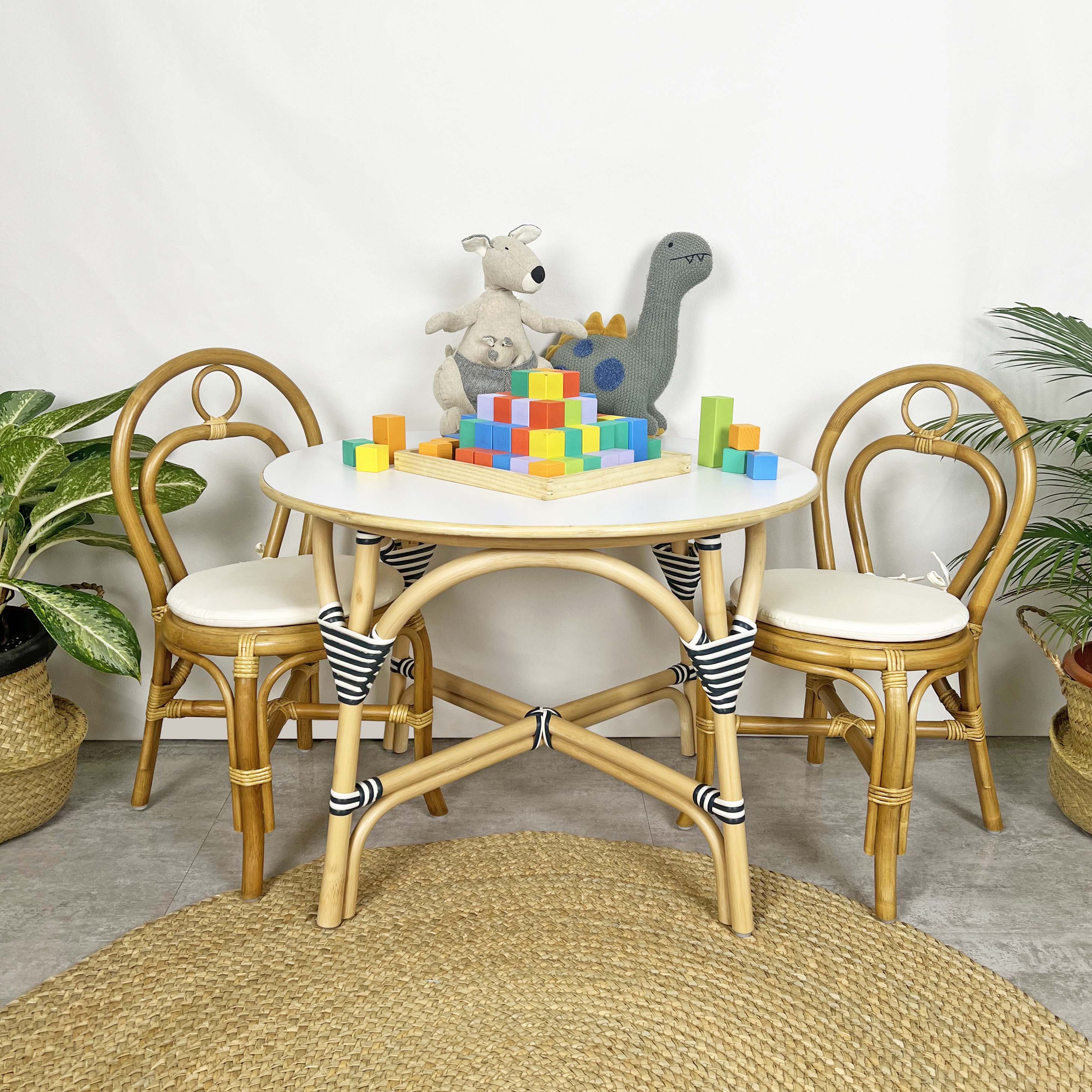 A handcrafted rattan wicker Aulia Kids Table & Set of 2 Amélie Kids Chairs by MOMIJI displayed in a playroom setting, with colorful toys placed on top of the table