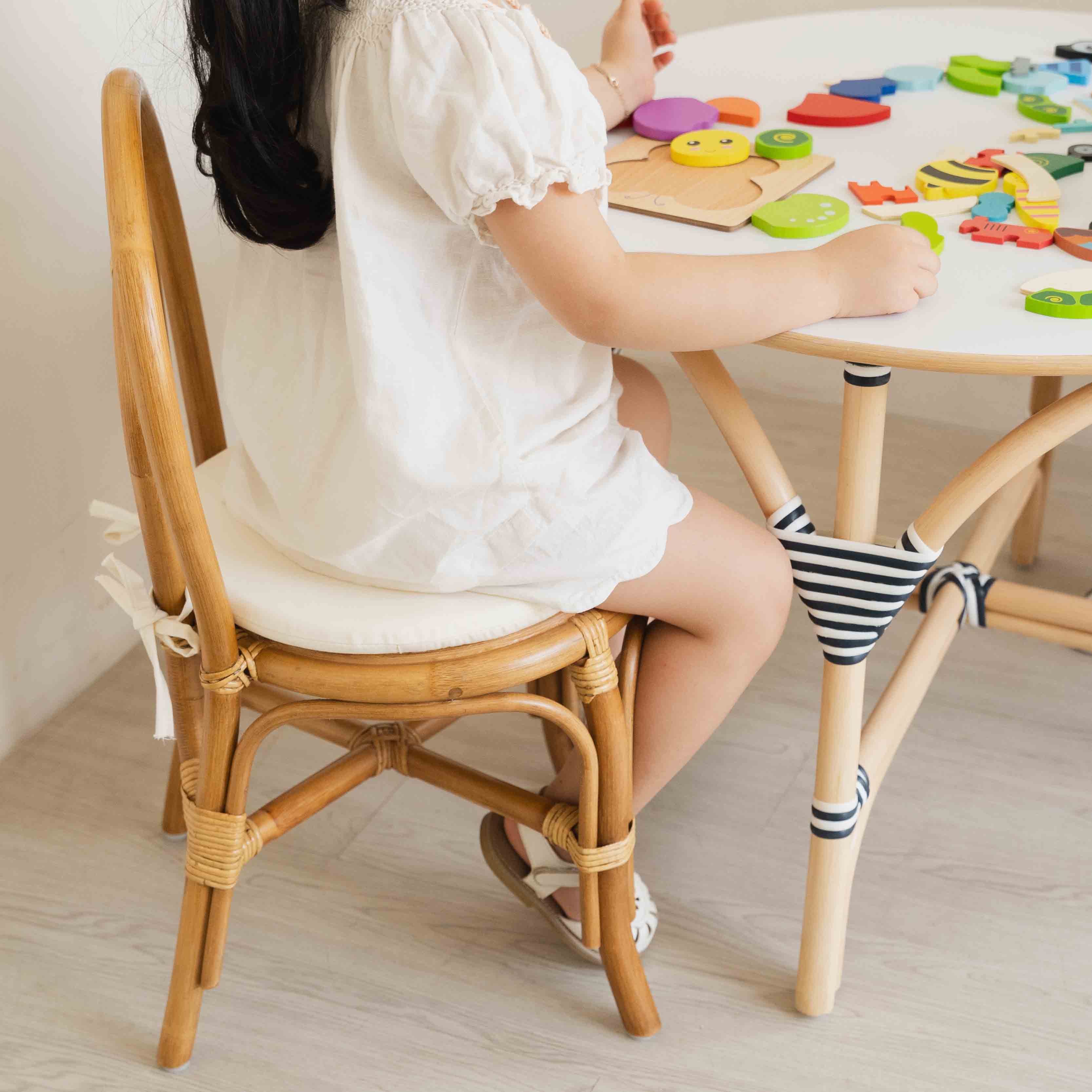 Child sitting on the handcrafted rattan wicker Amélie Kids Chair by MOMIJI while playing with colorful puzzle toys at the Aulia Kids Table, highlighting the sturdy and child-safe design of the rattan chair and table set