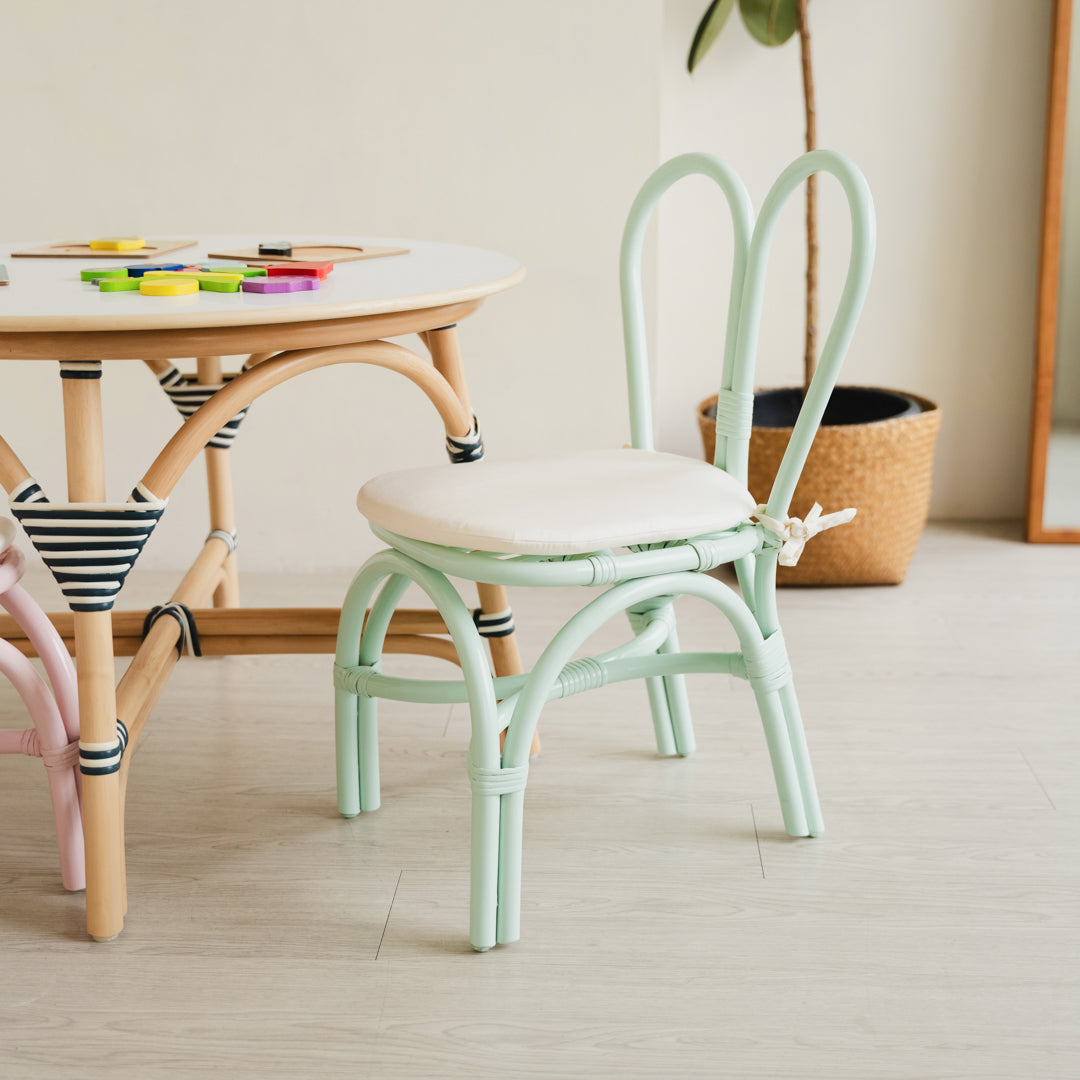 Handcrafted Mint Green rattan wicker Kids Bunny Chair by MOMIJI with a comfortable white cushion, styled with an Aulia Kids Table featuring a sturdy reinforced edge for added strength and stability, alongside toys in a bright playroom