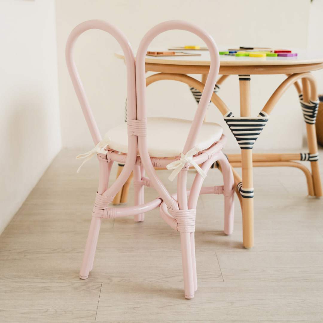 Back view of the handcrafted Pink rattan wicker Kids Bunny Chair by MOMIJI, showcasing its whimsical bunny-ear backrest, styled with an Aulia Kids Table and toys in a playful children's room.