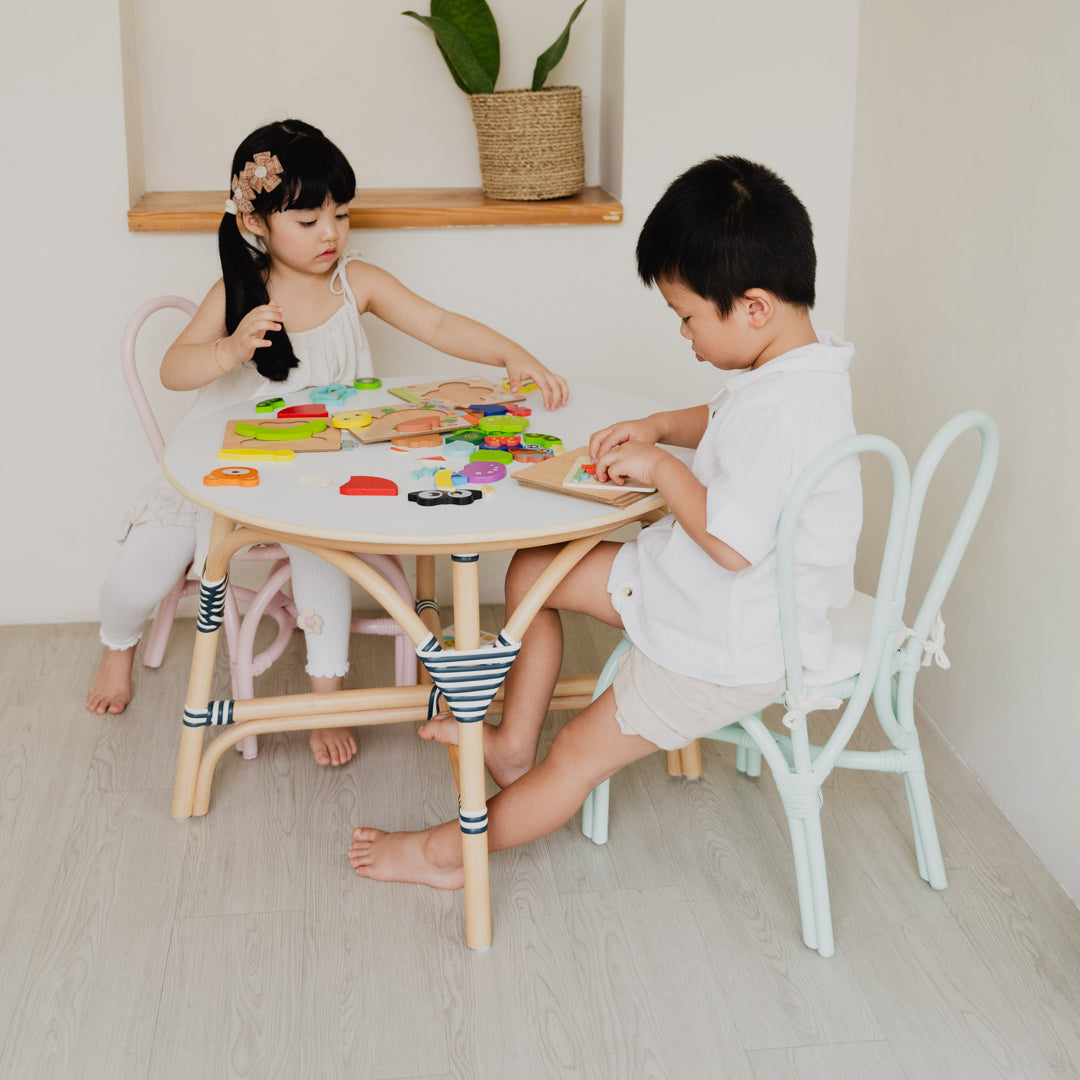 Children enjoying playtime on handcrafted Pink and Mint Green rattan wicker Bunny Chairs by MOMIJI, sitting at an Aulia Kids Table in a bright and cheerful children's room