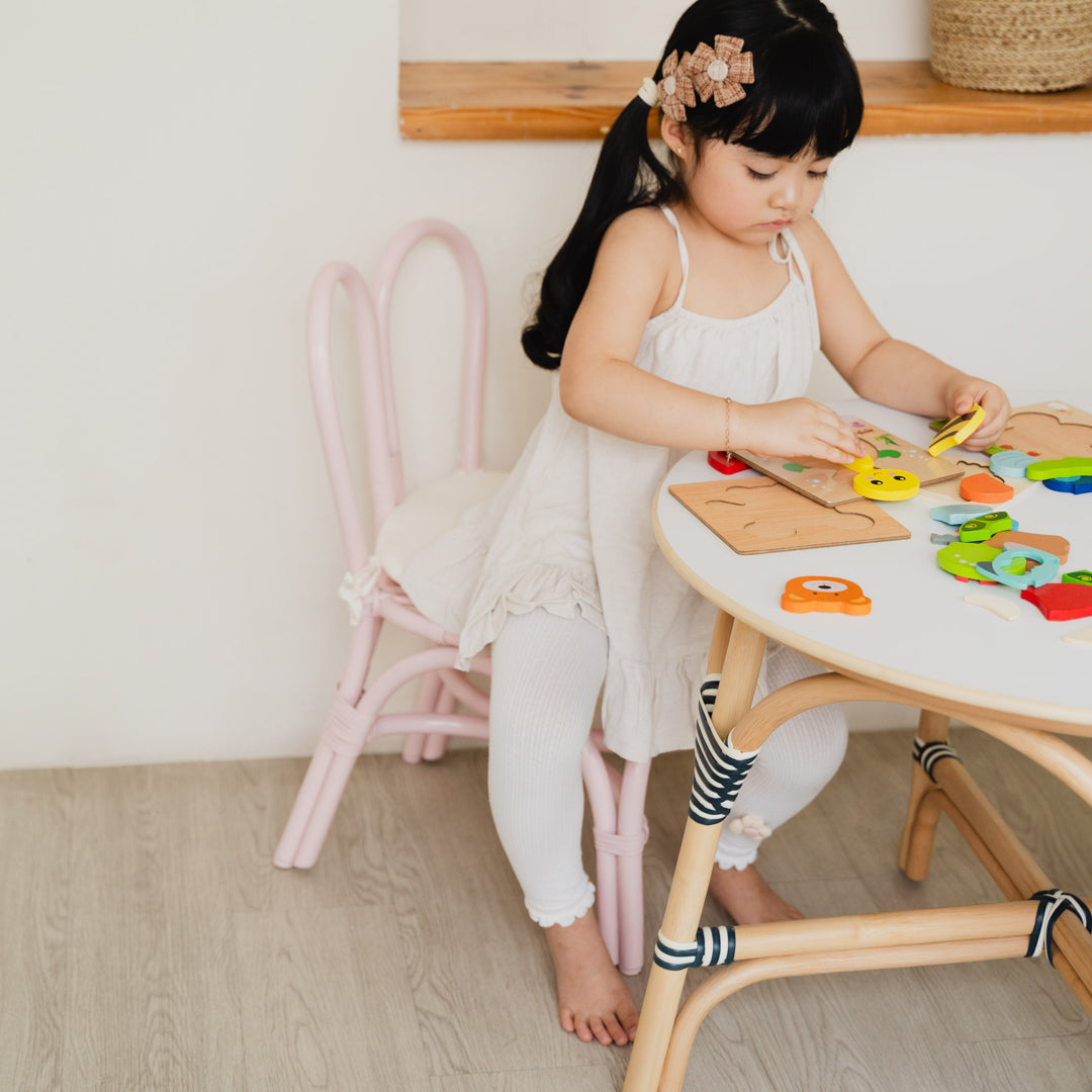 Child sitting on the Pink handcrafted rattan wicker Bunny Chair by MOMIJI while playing with colourful toys at an Aulia Kids Table in a playful children's room.