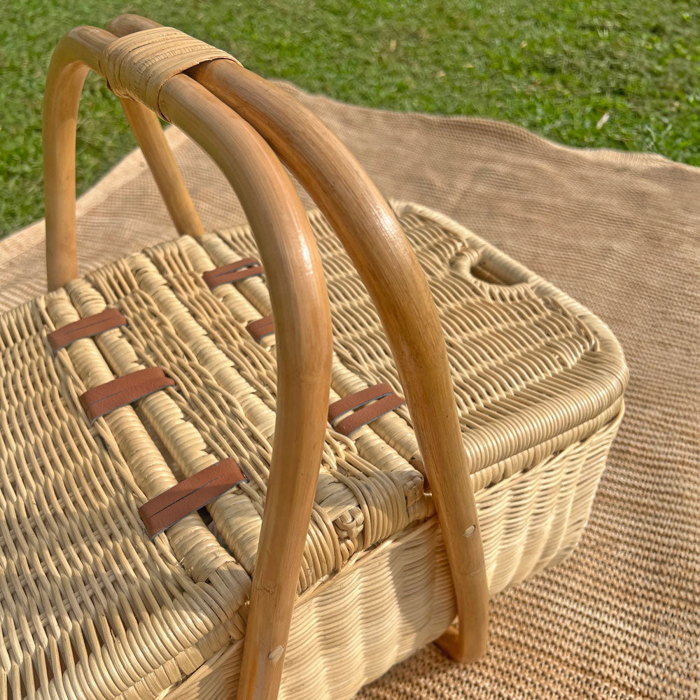 Aurelie rattan picnic basket by MOMIJI with handles on a grassy background.