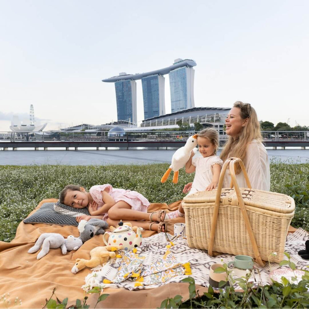 Woman and child sitting on a blanket with toys near an Aurelie rattan picnic basket by MOMIJI, Marina Bay Sands in the background.