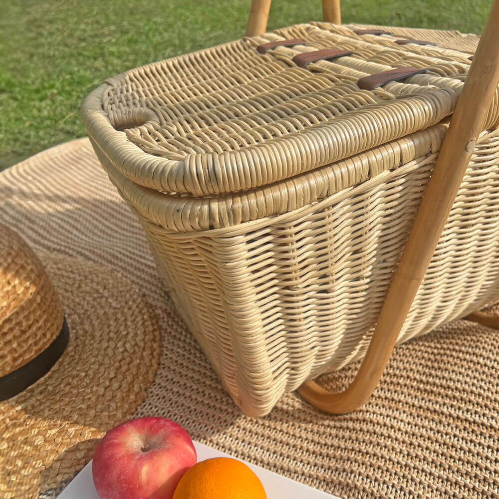 Aurelie rattan picnic basket by MOMIJI with a straw hat and fruits on a blanket outdoors.