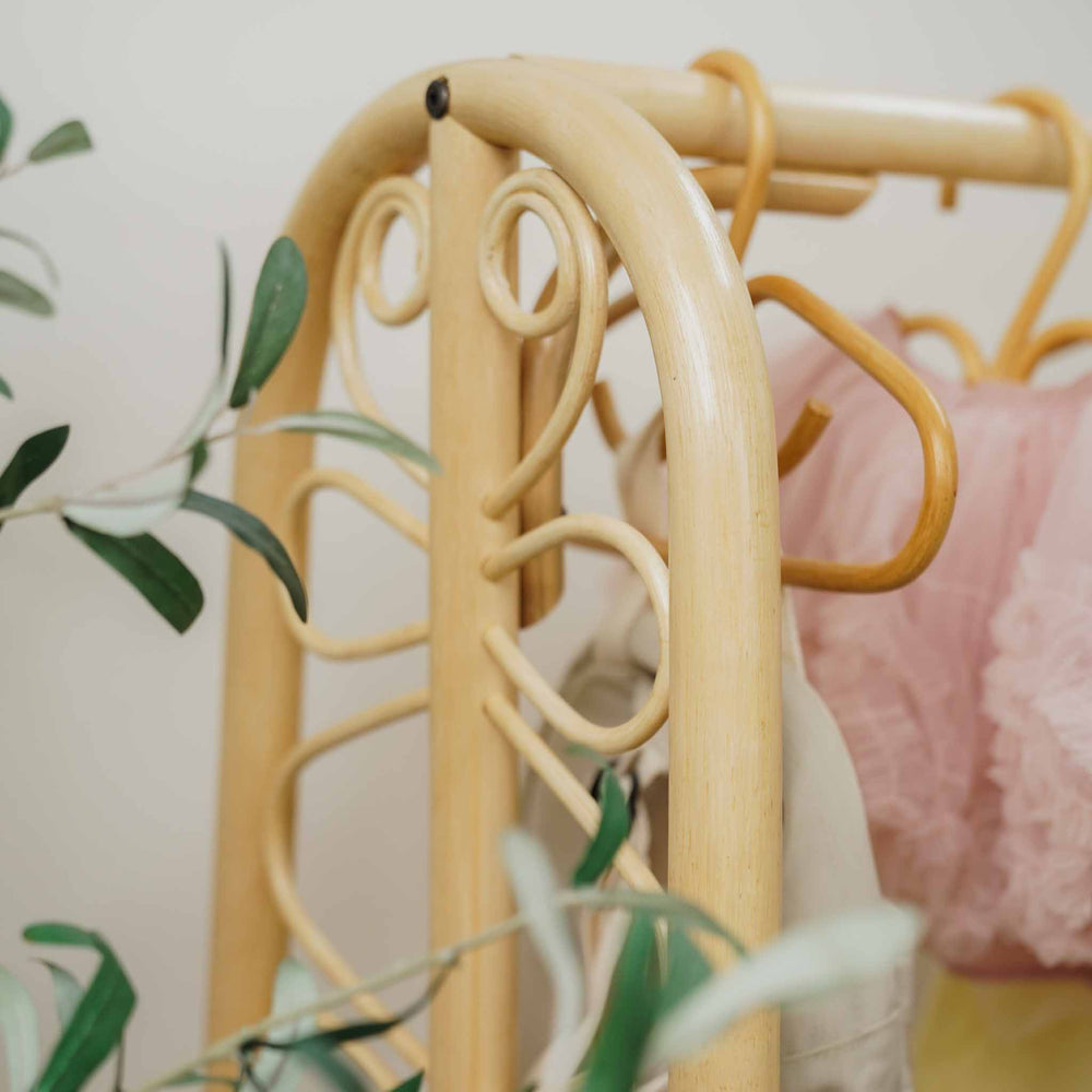 Close-up of the handcrafted natural rattan Belle Kids Montessori Clothing Rack by MOMIJI, highlighting its decorative curved scrollwork, sturdy hanging rail, and easy-to-assemble construction.