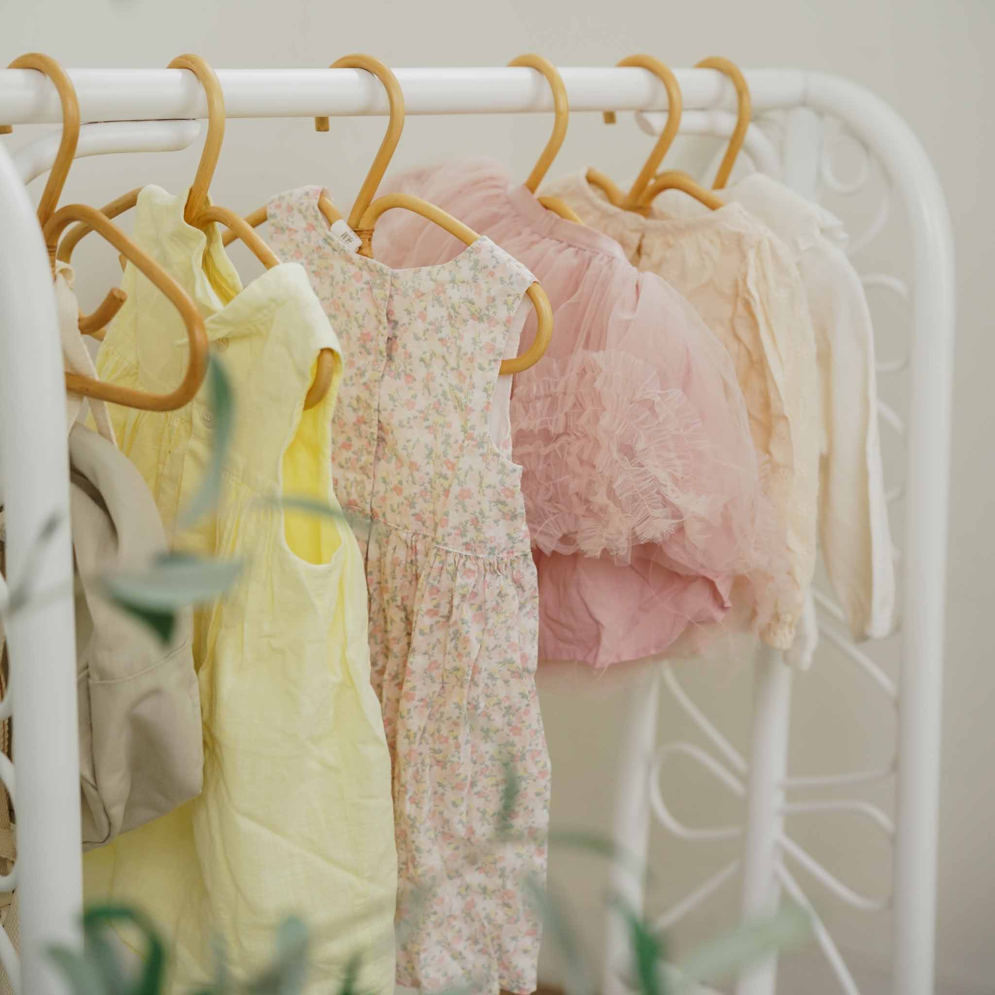 Close-up of pastel baby clothes hanging from the handcrafted white rattan Belle Kids Montessori Clothing Rack by MOMIJI, highlighting the child-friendly hanging rail designed for easy access and organisation.