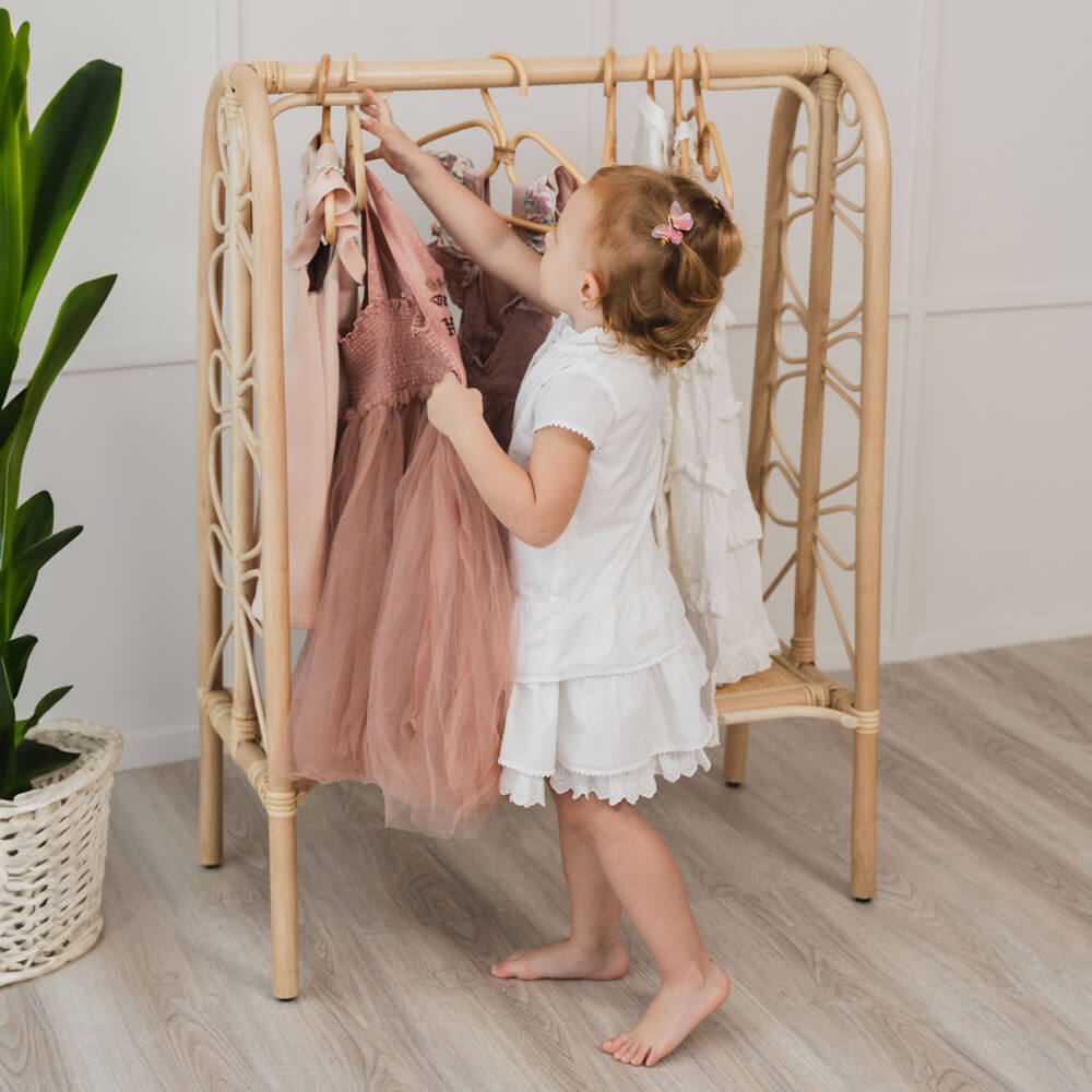 Child playing with the Belle Kids Montessori Clothing Rack by MOMIJI holding dresses in a room with a plant.
