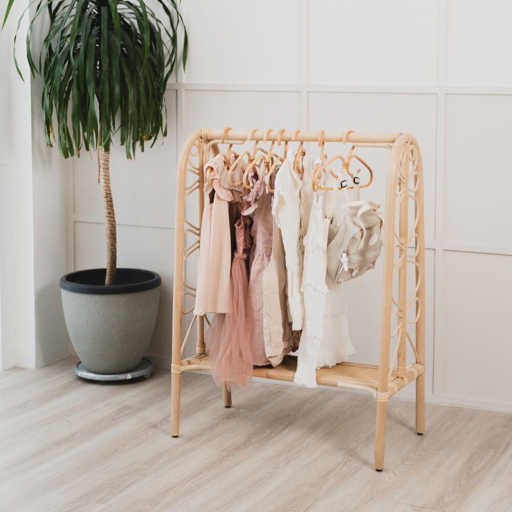 Belle Kids Montessori Clothing Rack by MOMIJI with hanging clothes placed beside a potted plant on a wooden floor.