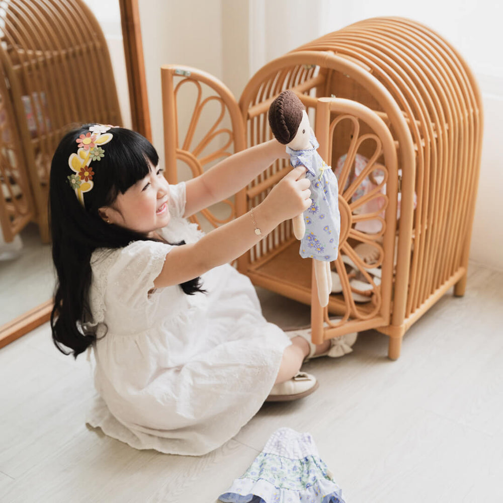 Happy child holding a doll beside the Blossom Doll Closet by MOMIJI indoors.
