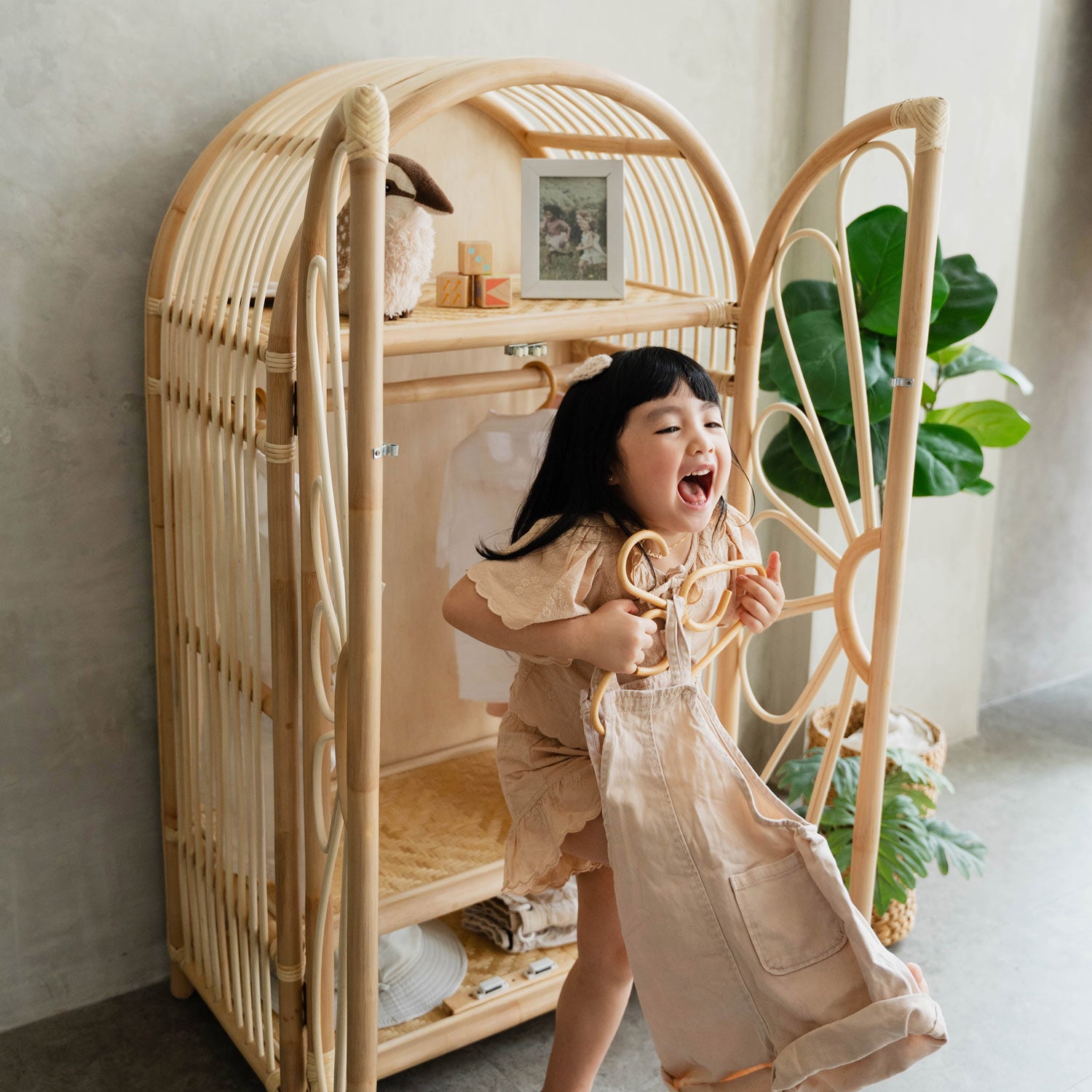Child holding up the clothes she took off the rattan wicker wardrobe cabinet rack in her bedroom