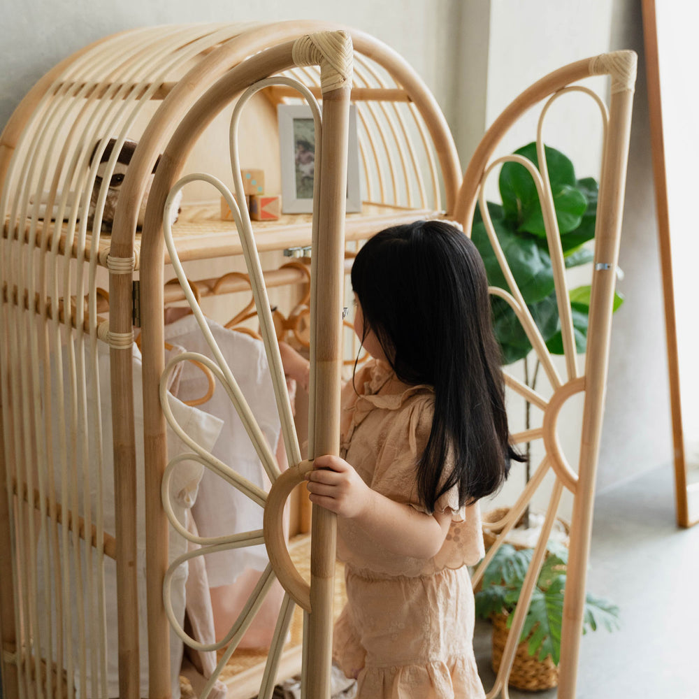 Child reaching inside a wicker rattan wardrobe cabinet to grab the kids clothes hung on the rack 