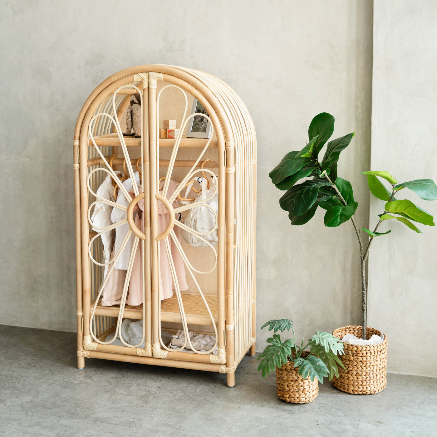 Handcrafted Rattan Wicker wardrobe cabinet with children's clothes and plants in a room setting