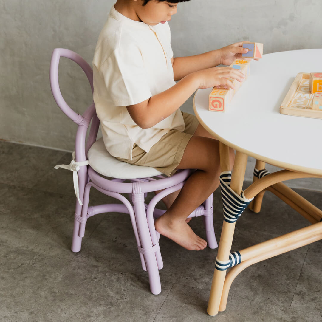 Child sitting on a purple Butterfly Kids Chair by MOMIJI, playing with blocks at a small table in a bright kids room.