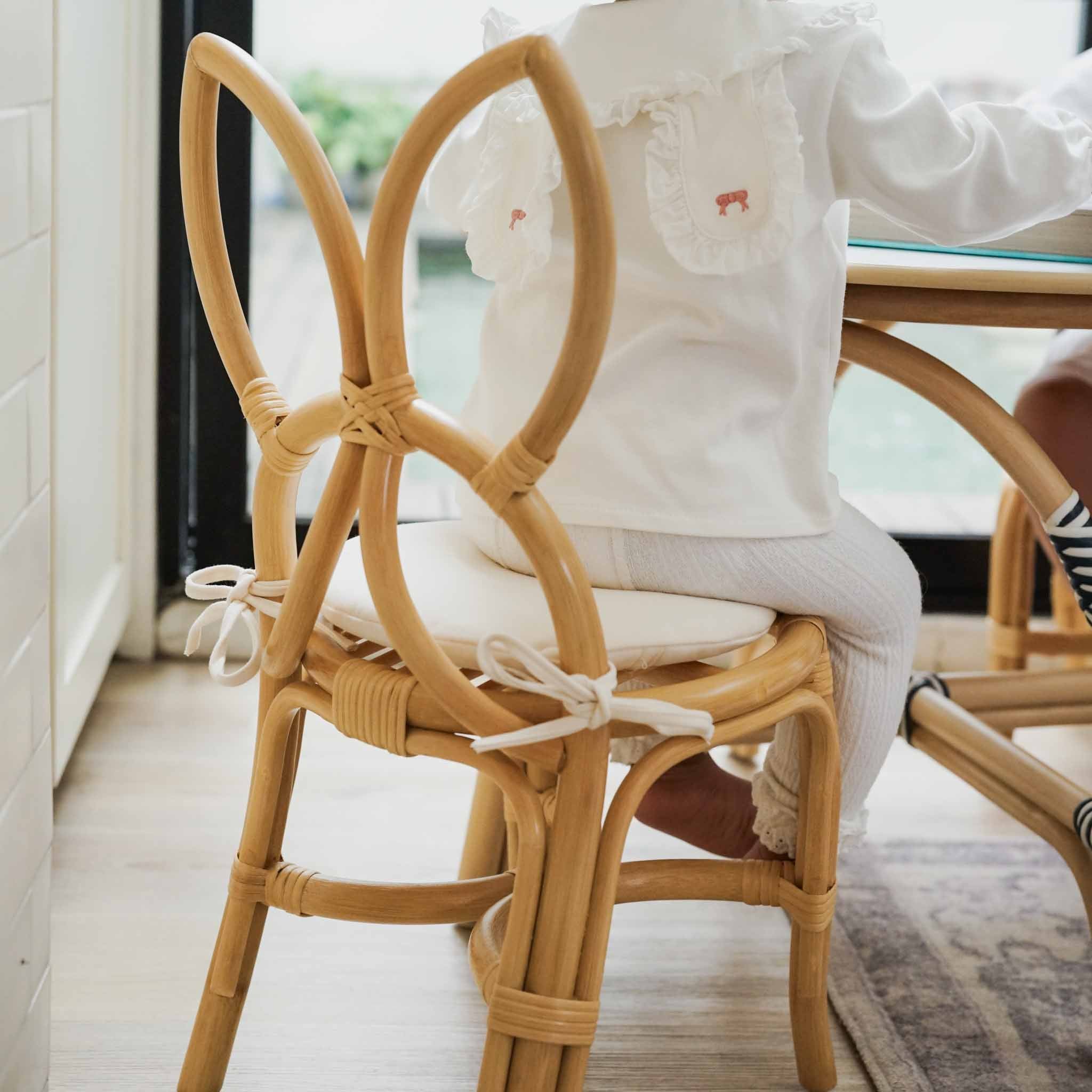 Back view of a child sitting comfortably on a handcrafted natural rattan wicker Butterfly Kids Chair with a soft removeable cushion, paired set with the Aulia Kids Table (Medium) by MOMIJI in a Montessori-inspired playroom.