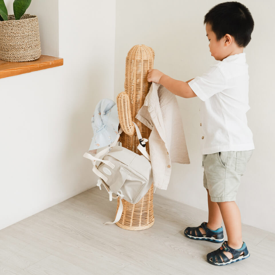 Child organizing clothes on a handcrafted Cactus Kids Coat Light Stand by MOMIJI in a kids room, combining playful design with practical storage.