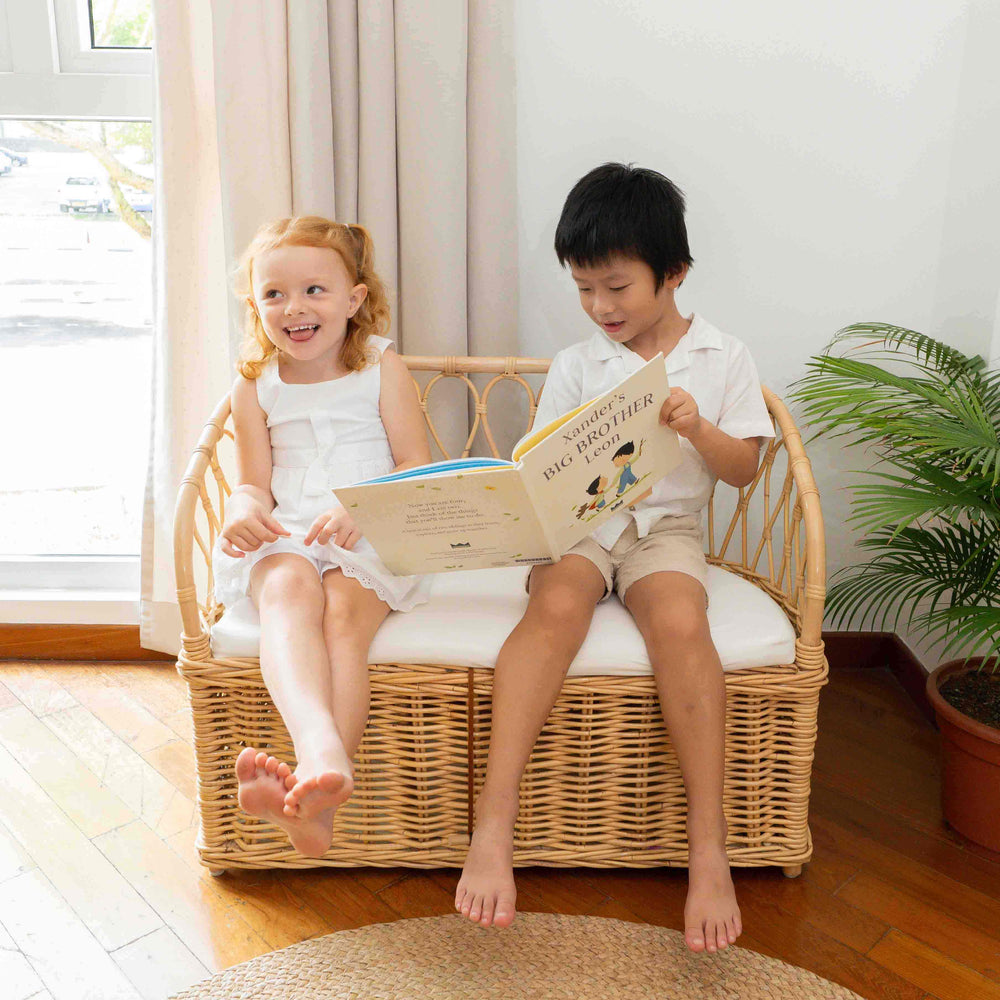 Two children sitting on the Callie Kids’ Storage Couch by MOMIJI reading a book indoors.