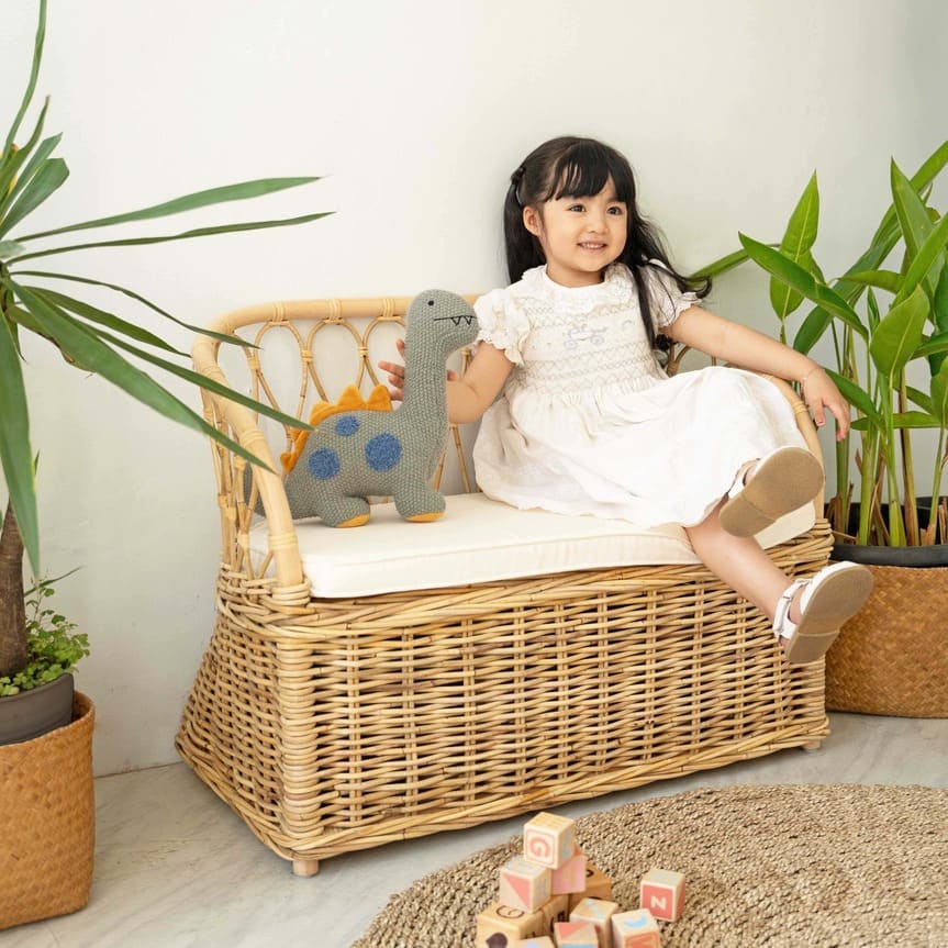 Child sitting on the Callie Kids’ Storage Couch by MOMIJI surrounded by toys and indoor plants.