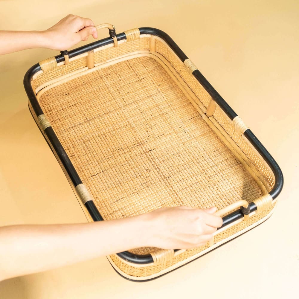 Top view of a hand holding the Coco Serving Tray by MOMIJI, showing its woven rattan surface.
