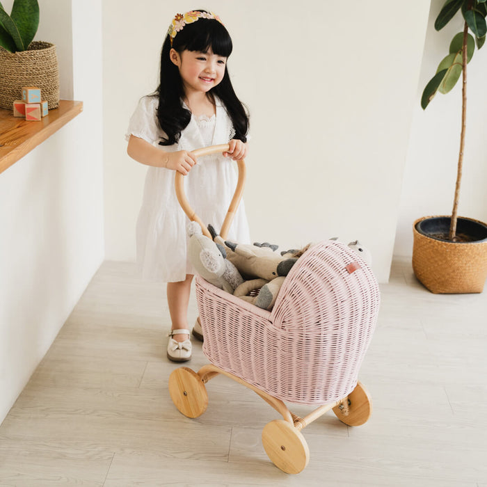 Young girl pushing the handcrafted pink rattan wicker Colette Doll Stroller by MOMIJI, designed for pretend play and doll storage.