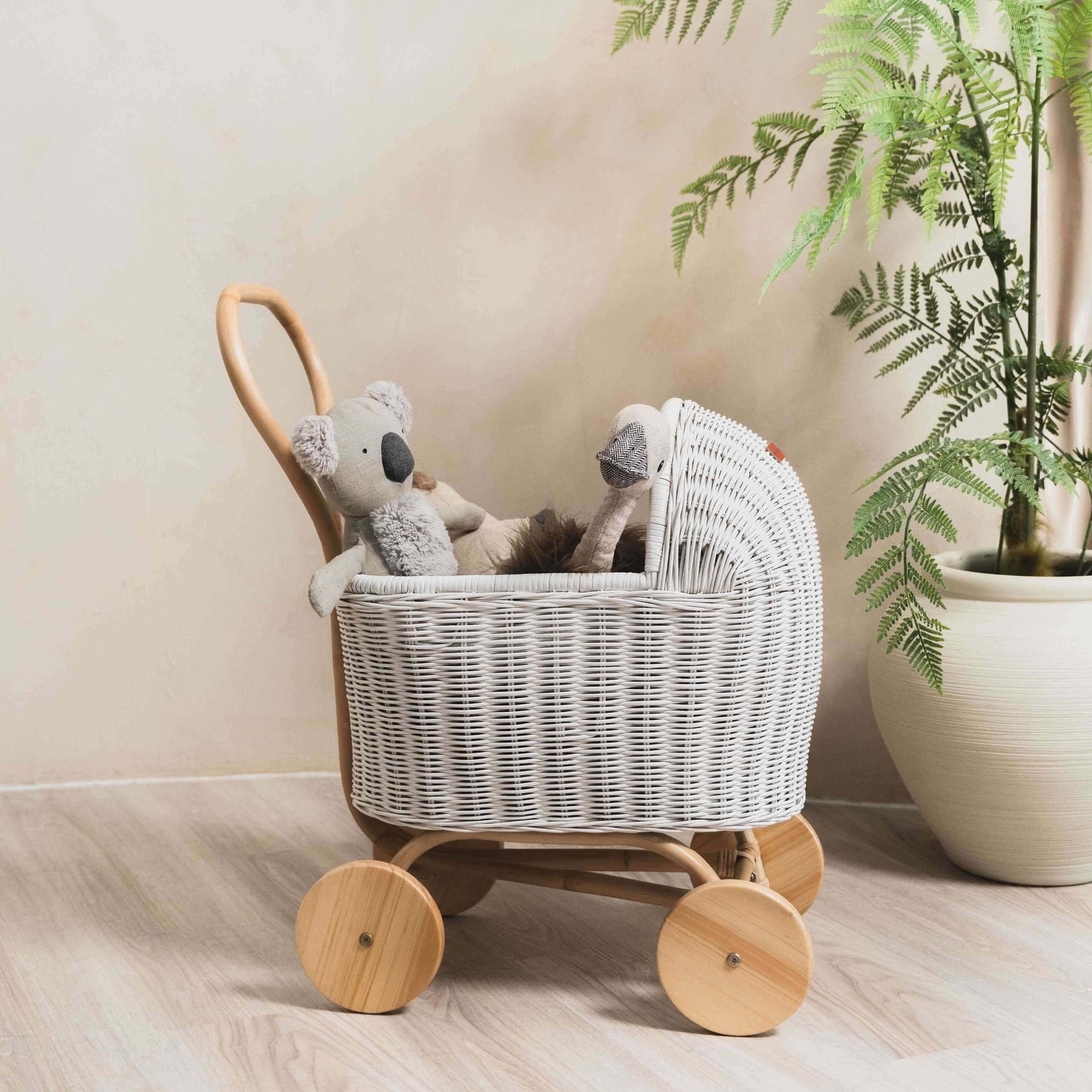 Side view of the Colette Doll Stroller by MOMIJI in white with a doll inside, styled in a room with plants.