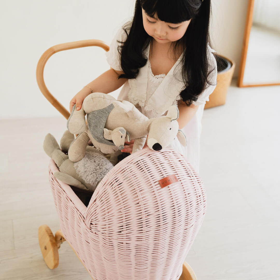 Child taking a stuffed toy from the handcrafted pink rattan wicker Colette Doll Stroller by MOMIJI during imaginative play.