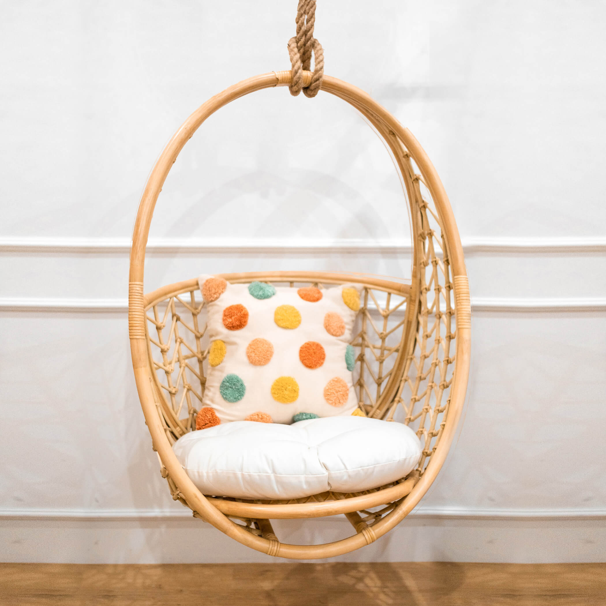 Front view of the Cross Hatch Hanging Chair by MOMIJI styled indoors with a white cushion and polka dot pillow.