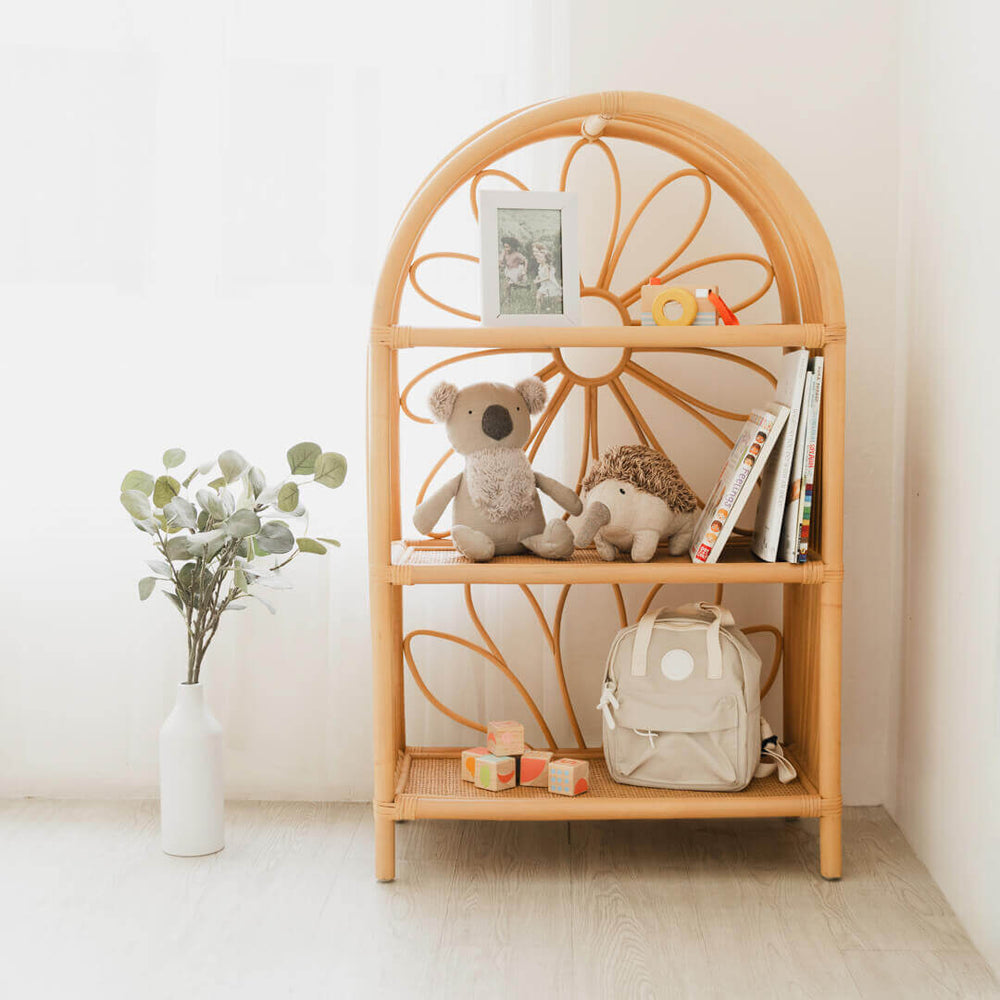 Daisy Arch rattan shelf by MOMIJI styled with toys, books, and a bag in a cozy room with indoor plants.