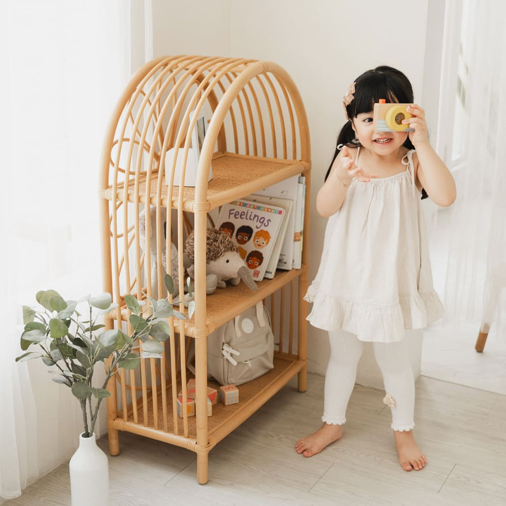 Child holding a toy camera next to the Daisy Arch Shelf by MOMIJI in a bright room.